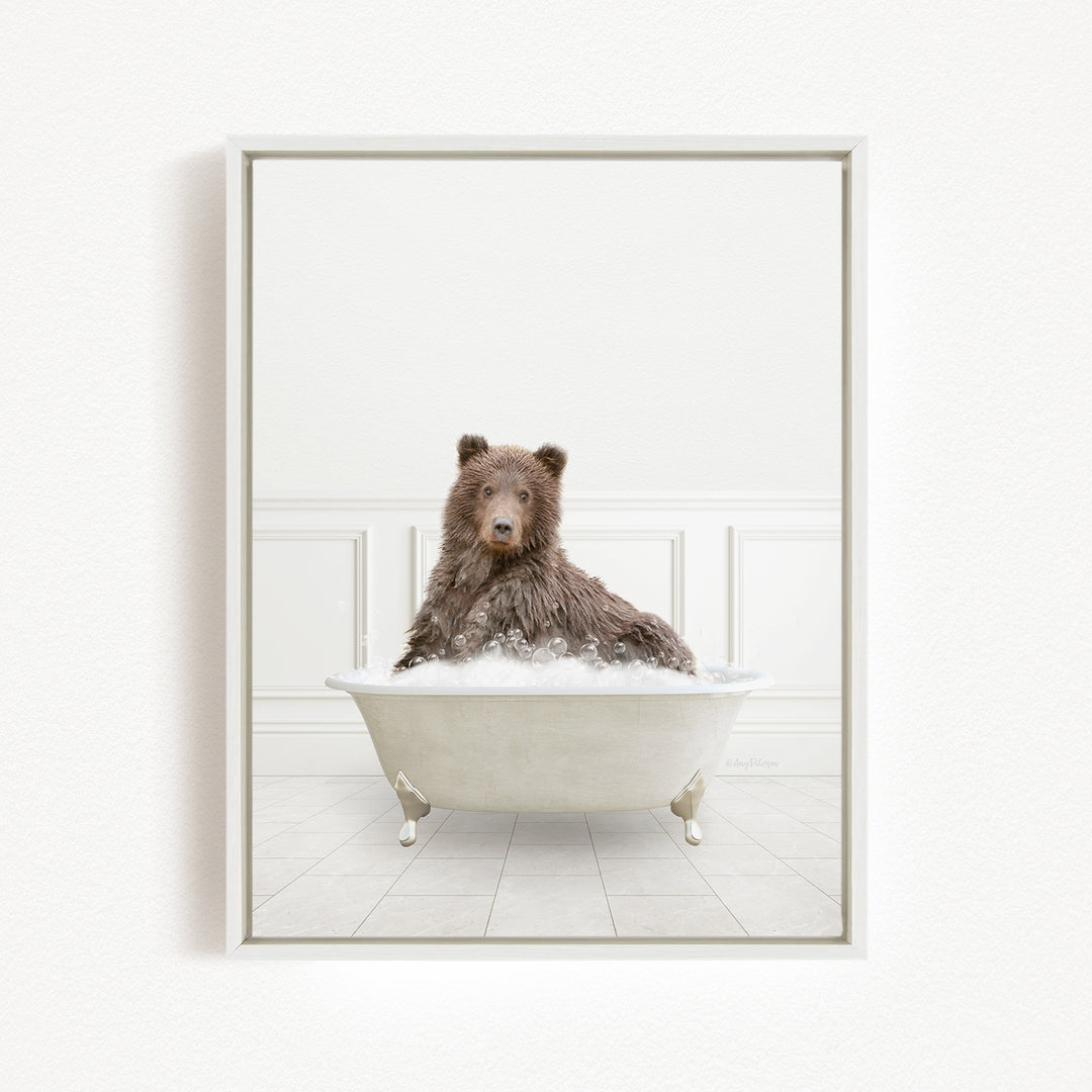 A brown bear sitting in a white bathtub filled with bubbles, looking directly at the camera.