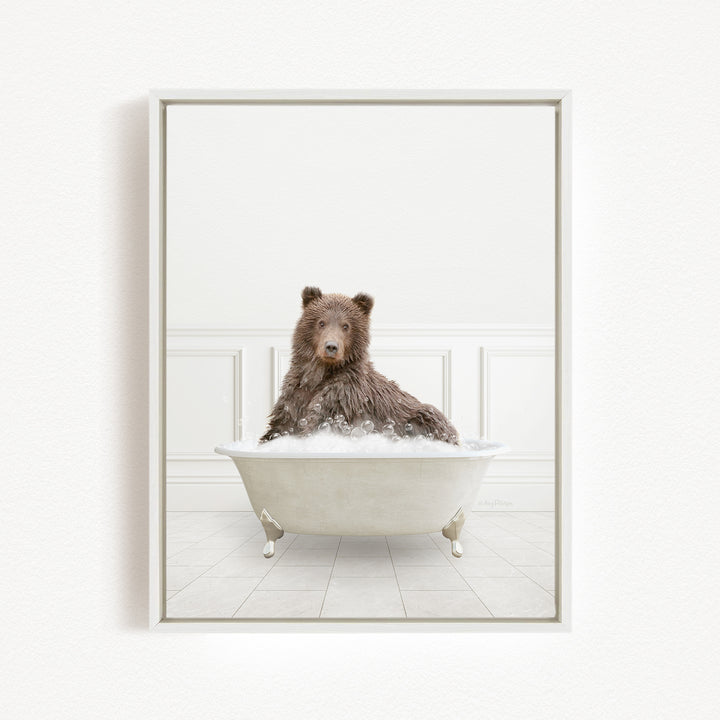 A brown bear sitting in a white bathtub filled with bubbles, looking directly at the camera.