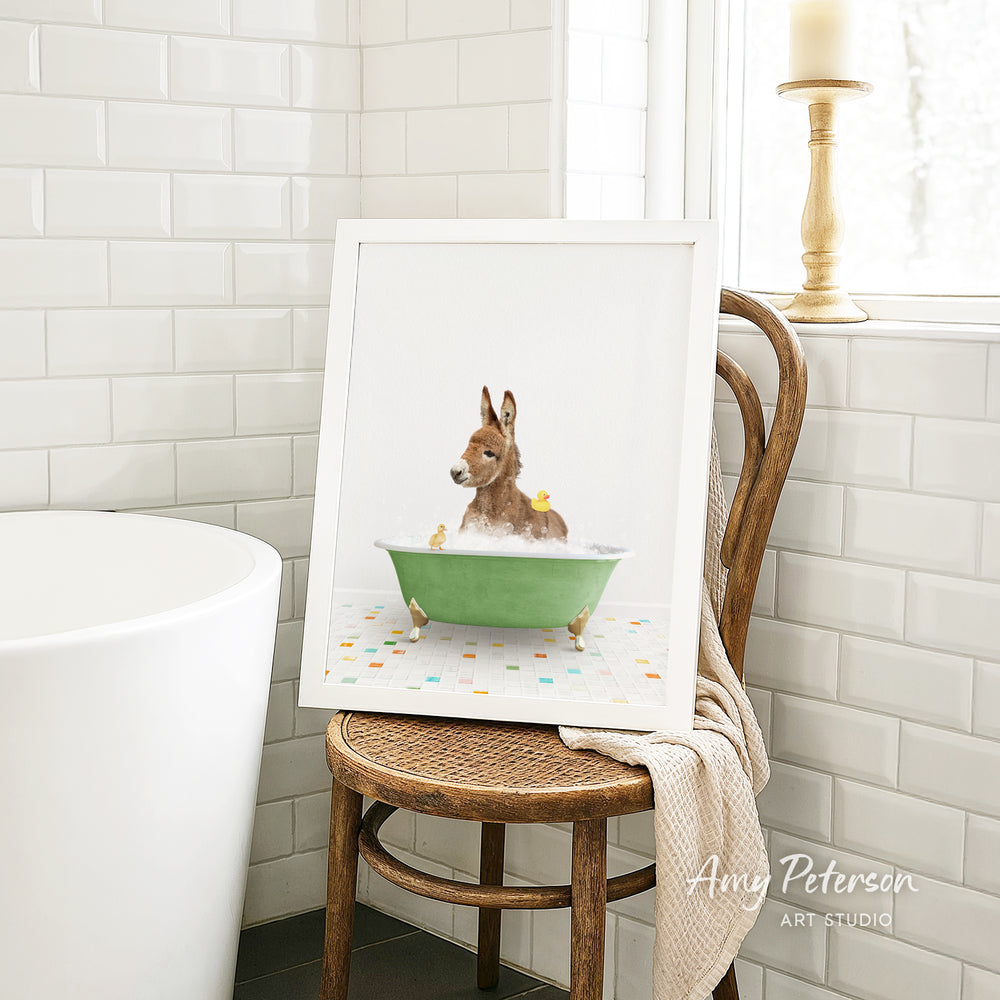 A framed image of a brown dog sitting in a green bathtub, surrounded by yellow rubber ducks, is displayed on a wooden chair in a bathroom setting.