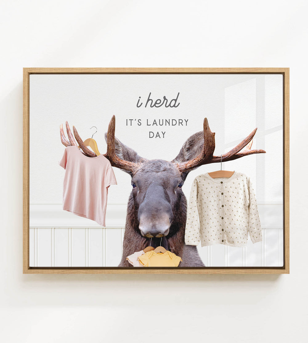 A framed image depicting a moose with antlers holding clothes, accompanied by the text "i herd, it's laundry day".