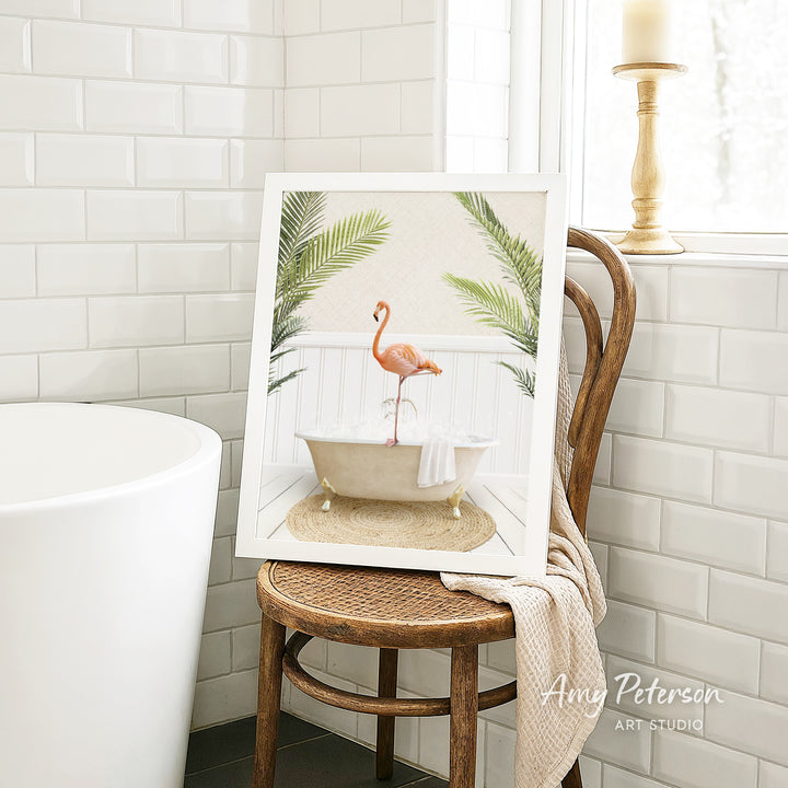 A framed image of a pink flamingo sitting in a bathtub, surrounded by tropical plants, is displayed on a wooden chair in a bathroom setting.