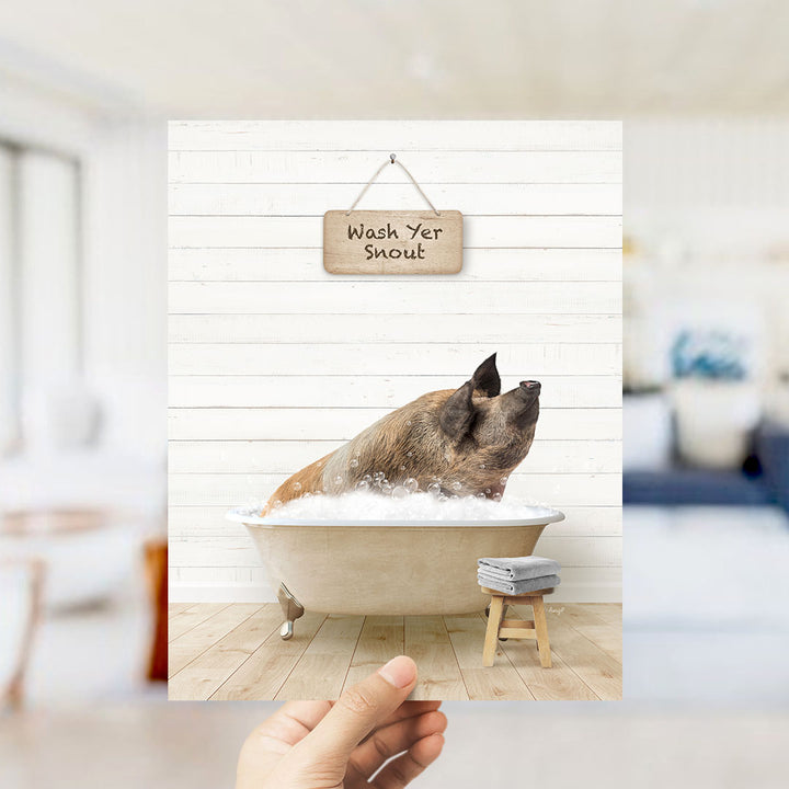 A hand holds up a framed image of a pig sitting in a bathtub, with a sign above that says "Wash Yer Snout".