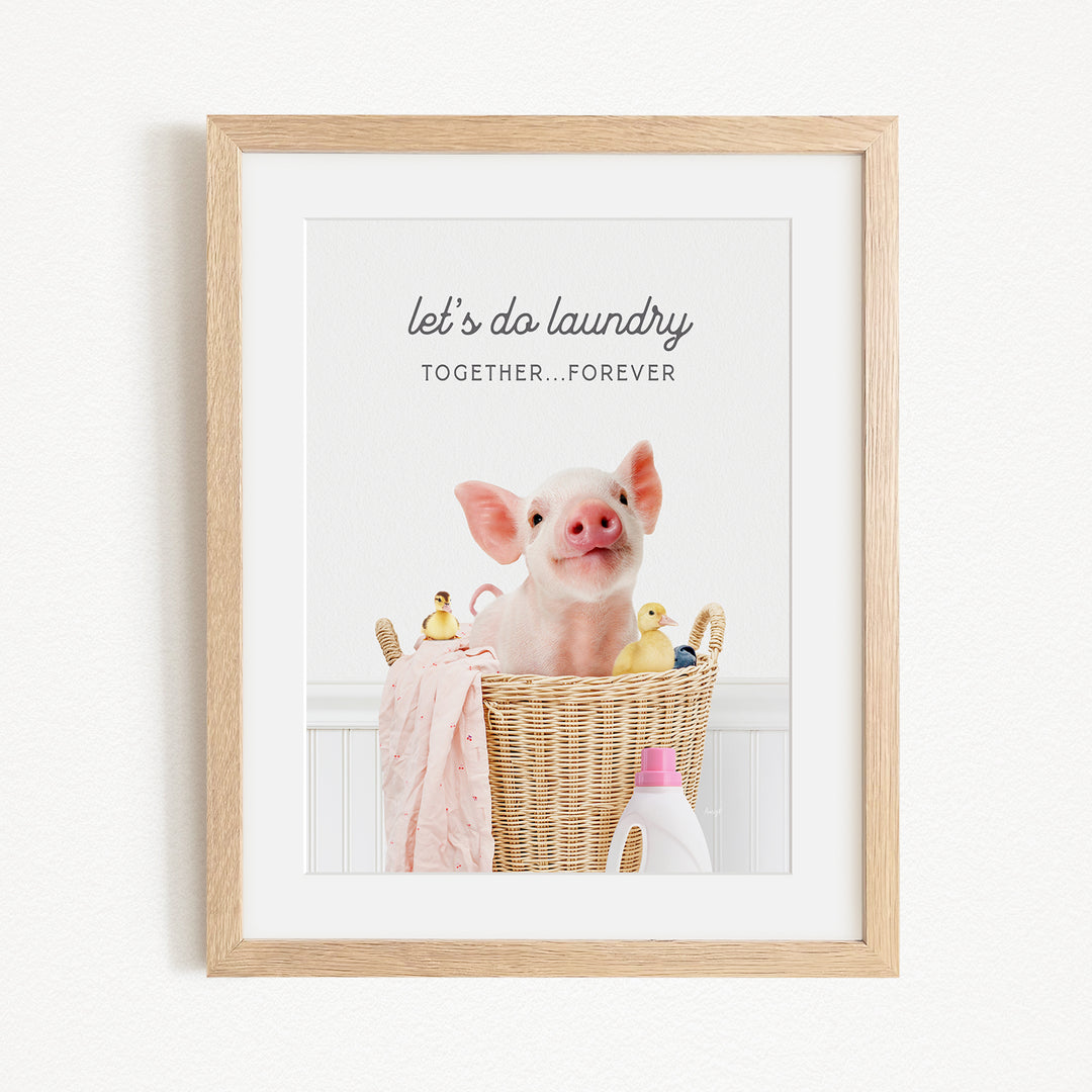 A framed image of a pig sitting in a wicker basket filled with rubber ducks, accompanied by the text "let's do laundry together forever".