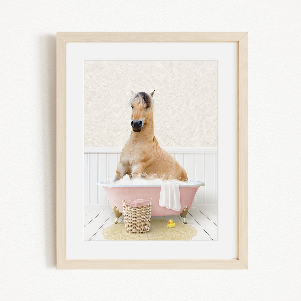 A light brown horse is sitting in a pink bathtub filled with water, surrounded by a yellow rubber duck and a basket.