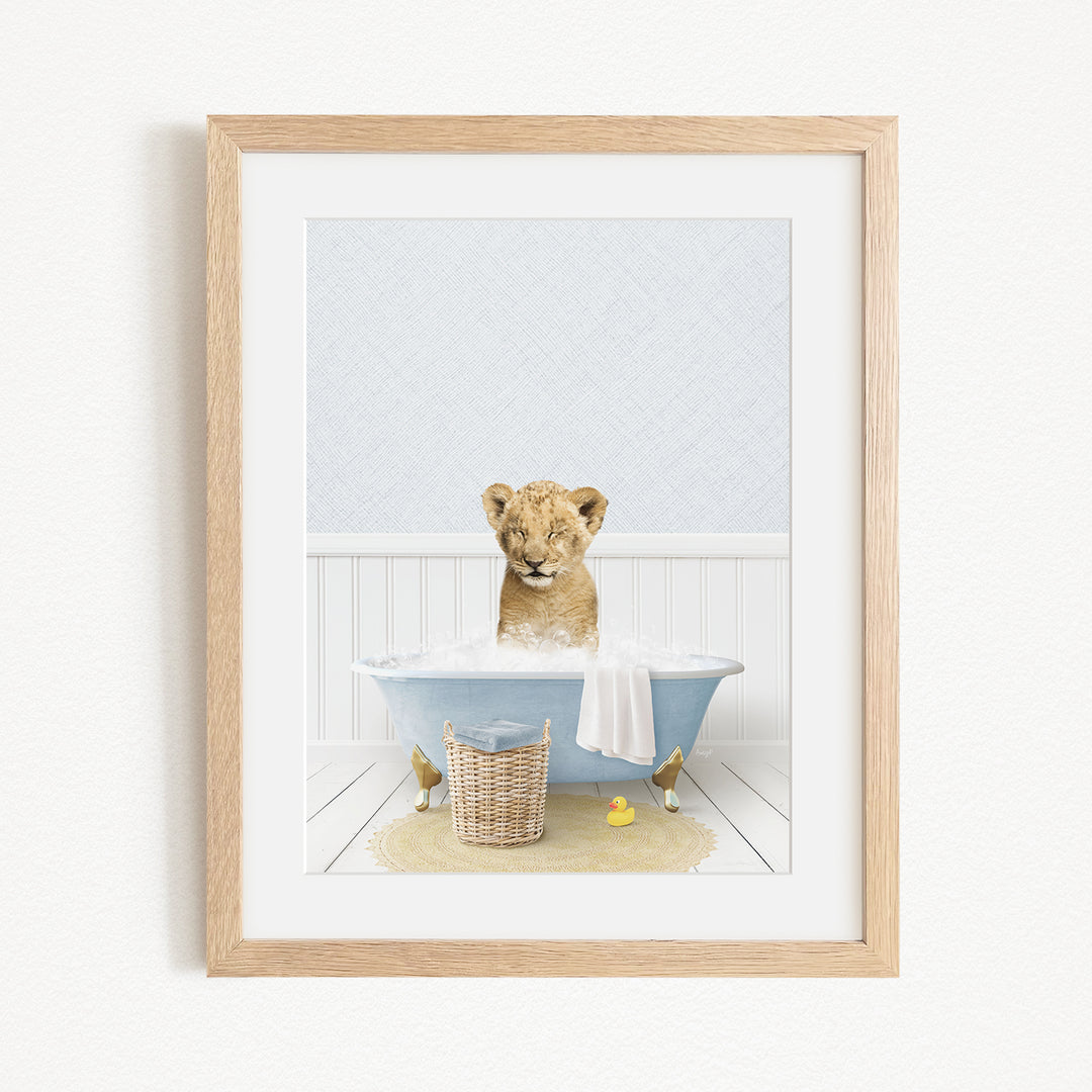 A young lion cub sitting in a blue bathtub filled with water, surrounded by rubber ducks and a basket.