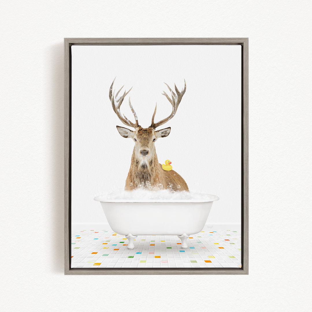 A deer with large antlers is sitting in a white bathtub filled with bubbles, with a yellow rubber duck perched on its head.