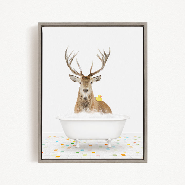 A deer with large antlers is sitting in a white bathtub filled with bubbles, with a yellow rubber duck perched on its head.