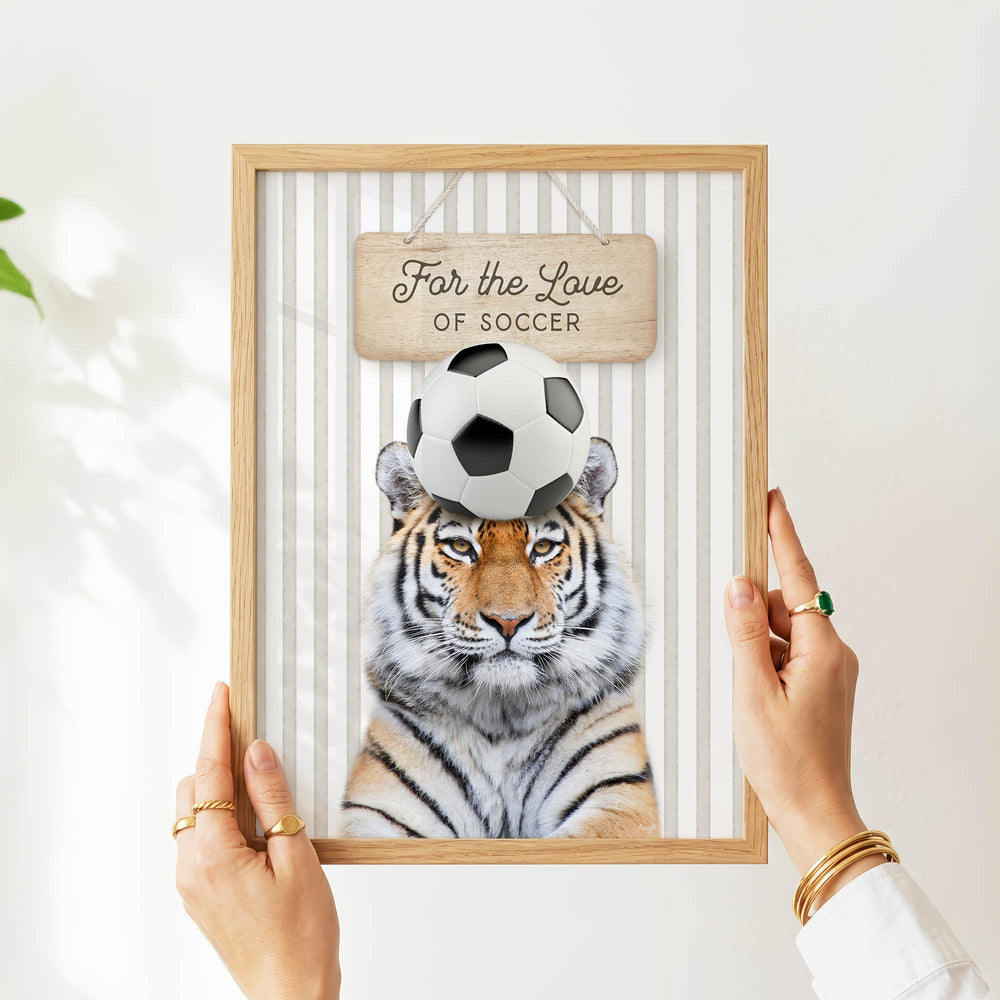 A person's hands are holding a framed picture of a tiger with a soccer ball on its head, displaying a humorous and playful image.