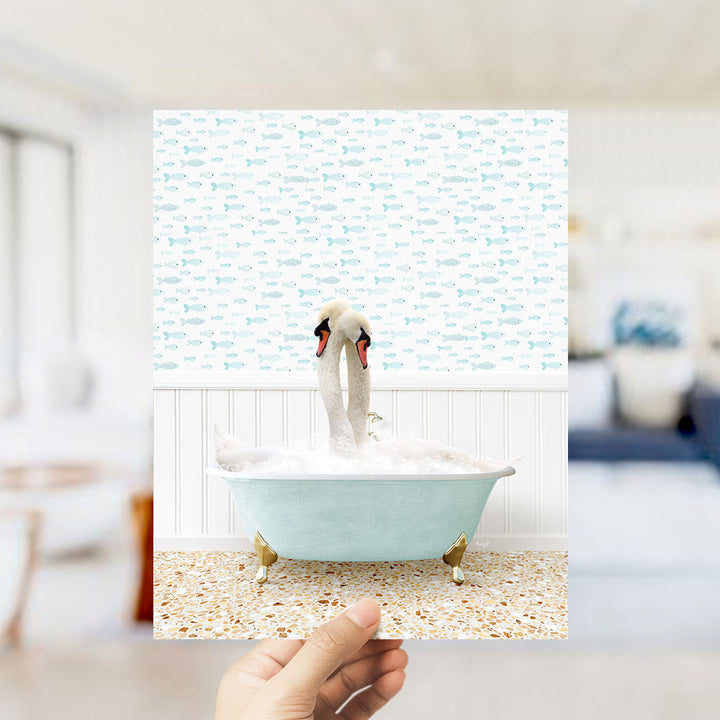 A hand holds up a framed image of a swan in a bathtub, surrounded by a pattern of fish.