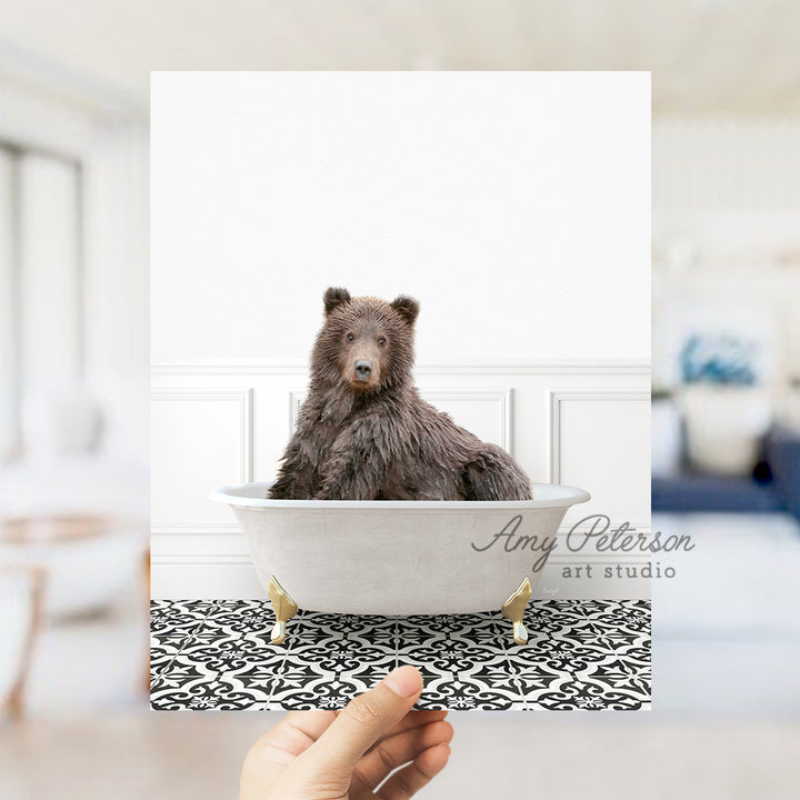 a hand holding a polaroid picture of a bear in a bathtub