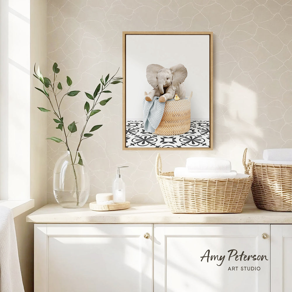 a framed photograph of an elephant sitting in a basket, hanging on a wall above a white cabinet with two woven baskets.