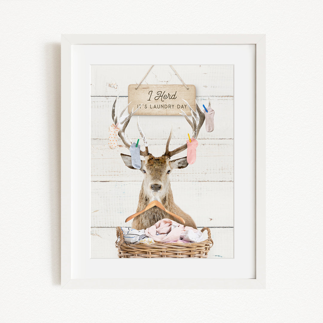 A framed image depicting a deer with antlers holding laundry, accompanied by a sign that reads "I herd it's laundry day".