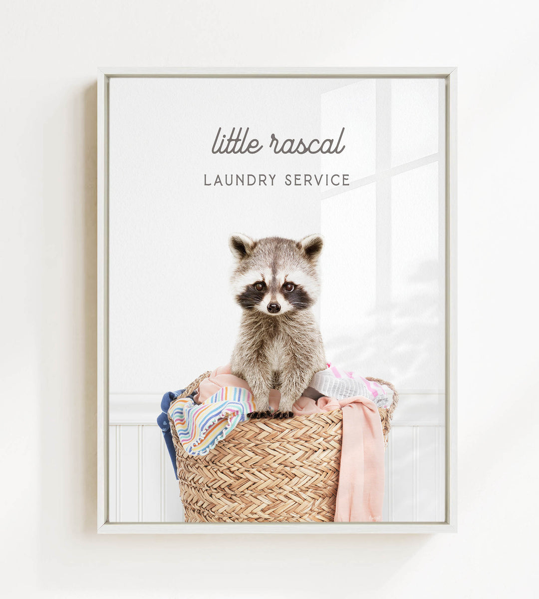 A raccoon sitting in a woven laundry basket, with the text "little rascal Laundry Service" displayed above the raccoon.