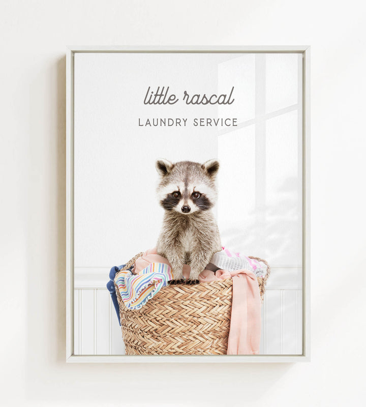 A raccoon sitting in a woven laundry basket, with the text "little rascal Laundry Service" displayed above the raccoon.