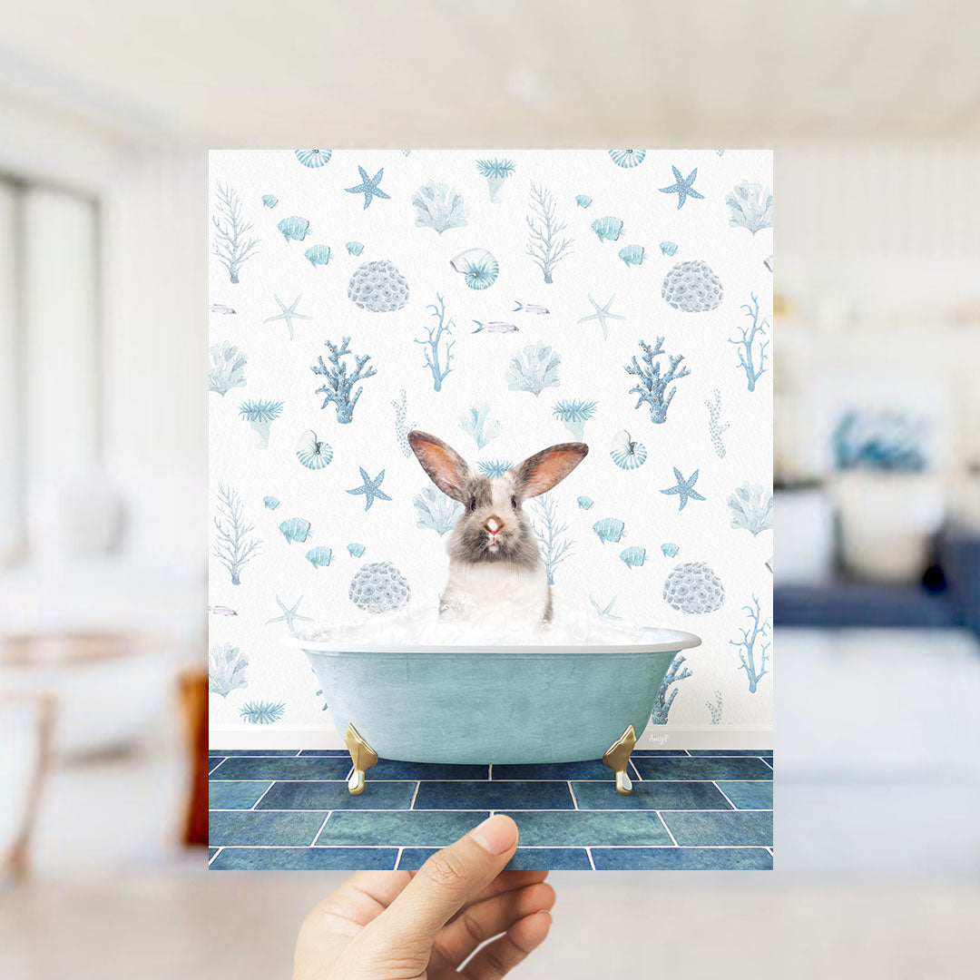 A hand is holding up a print featuring a rabbit sitting in a bathtub filled with bubbles, surrounded by a pattern of seashells, starfish, and other marine life.