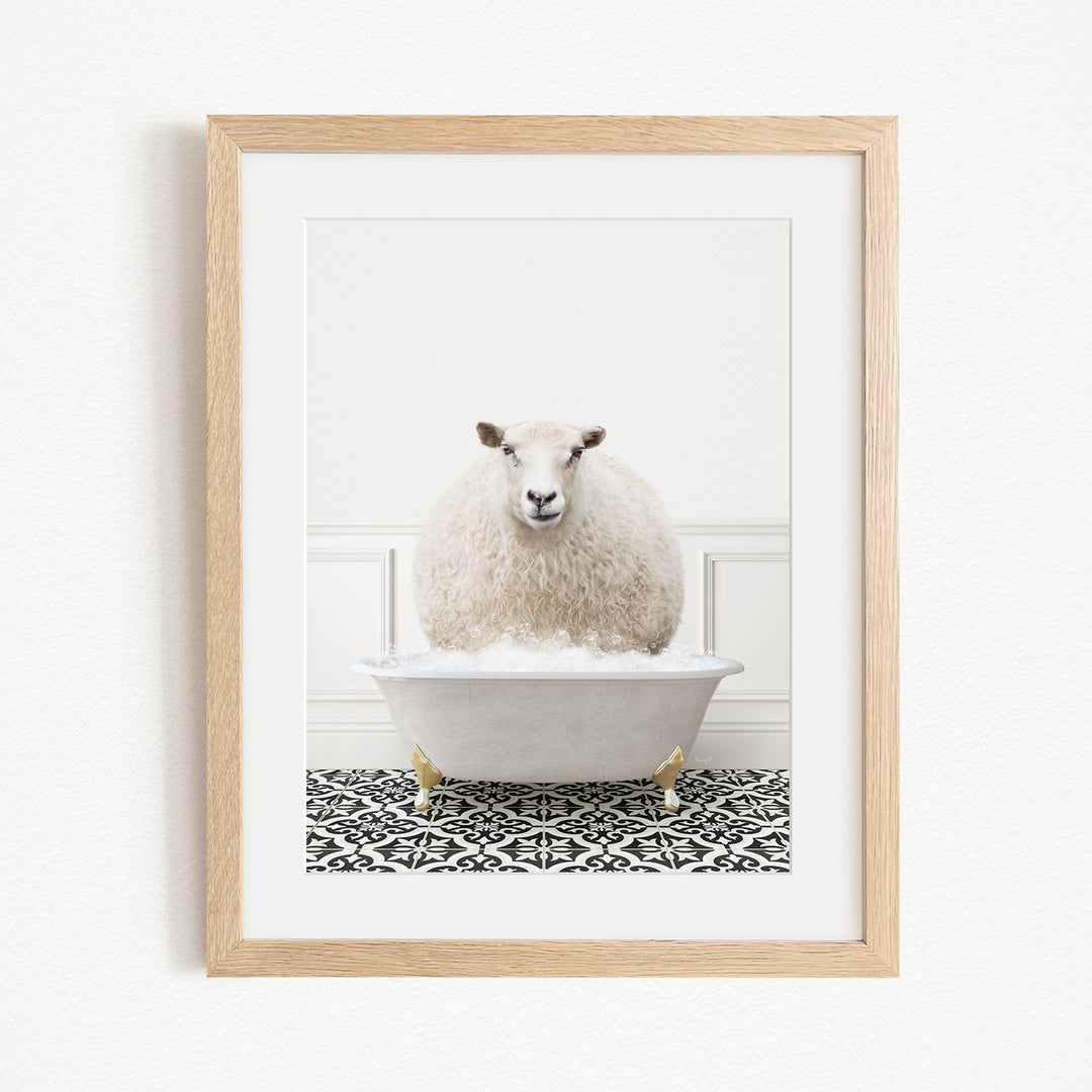 A fluffy white sheep sits in a white bathtub filled with bubbles, surrounded by a black and white patterned rug on a white wall.