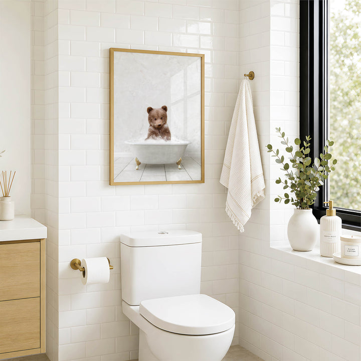 A bathroom with a white toilet, a framed image of a bear sitting in a bathtub, and a window with greenery on the sill.