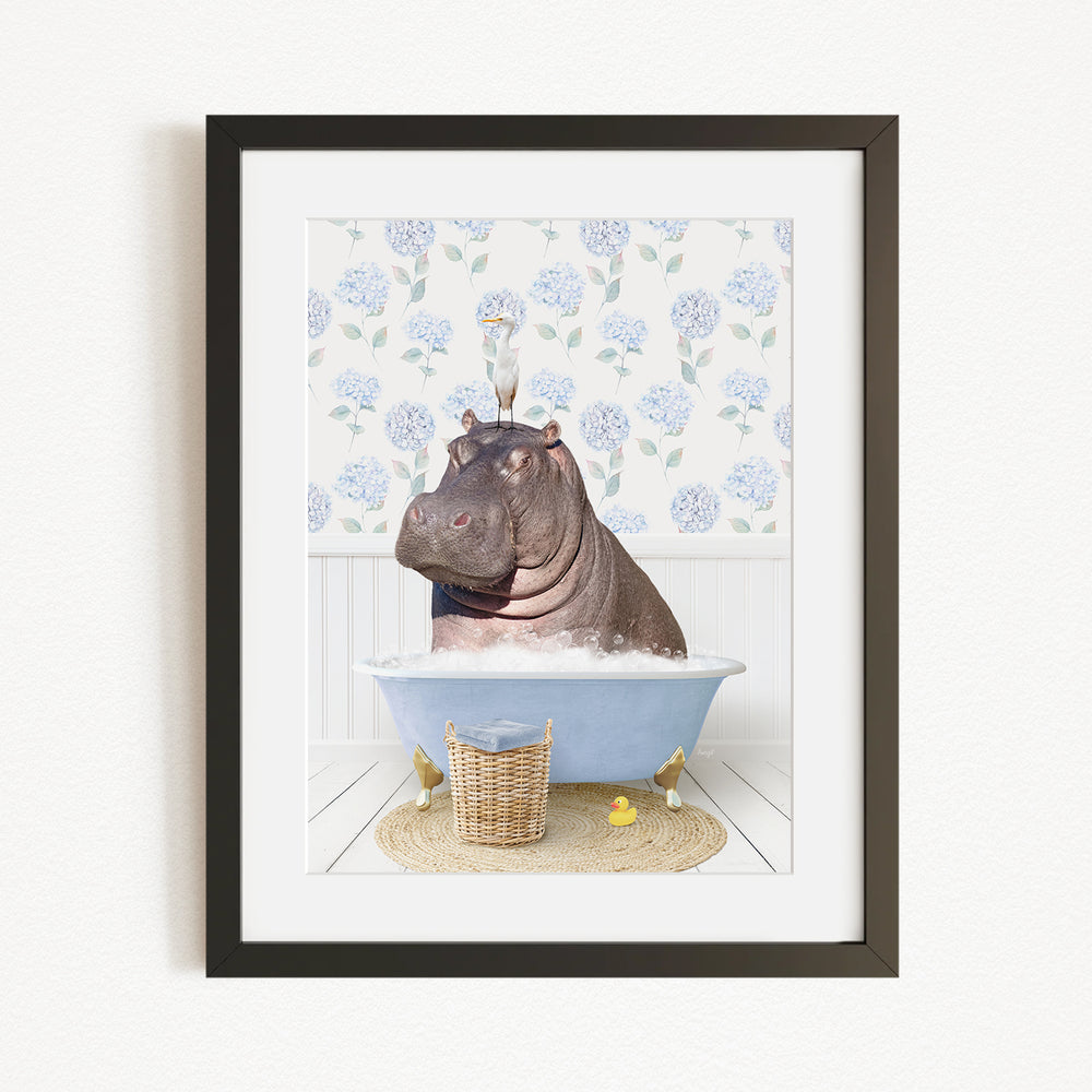 A framed image depicting a hippopotamus sitting in a bathtub filled with bubbles, surrounded by a floral patterned wall and a basket of rubber ducks.