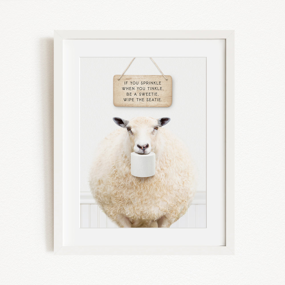 A framed image of a sheep holding a roll of toilet paper, with a wooden sign above it that reads "If you sprinkle when you twinkle, wipe the seagull".