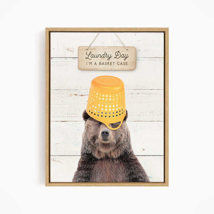 A framed image of a bear wearing a yellow basket on its head, with a sign above that says "Laundry Day I'm a basket case".
