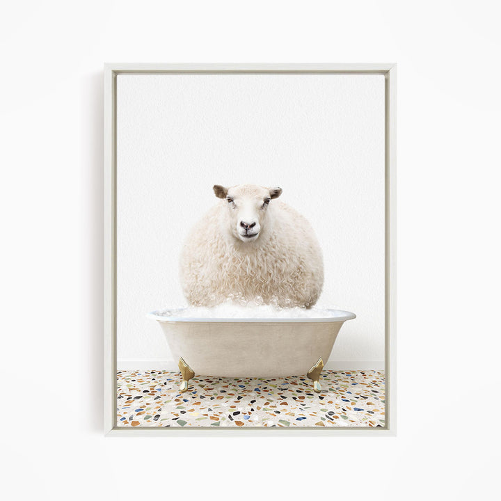 A fluffy white sheep sits in a white bathtub filled with bubbles, looking directly at the camera.