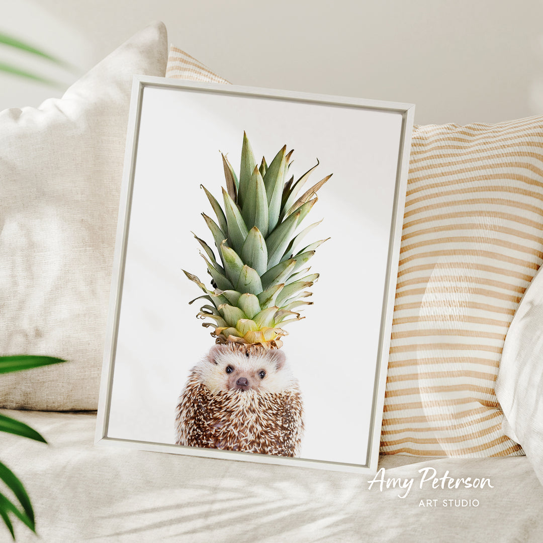A framed image of a hedgehog with a pineapple on its head, placed on a bed with striped pillows.