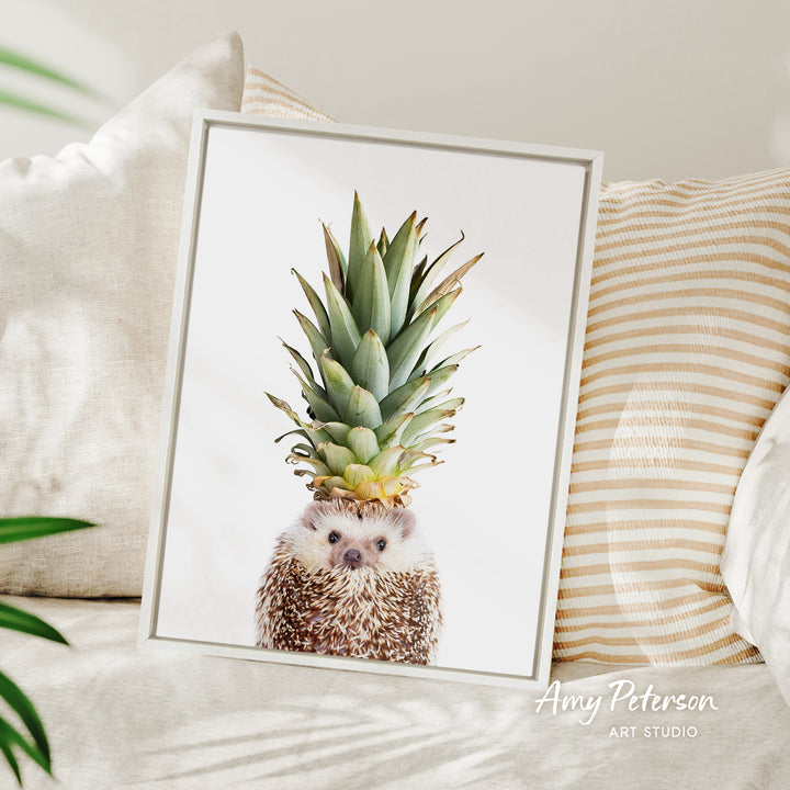 A framed image of a hedgehog with a pineapple on its head, placed on a bed with striped pillows.