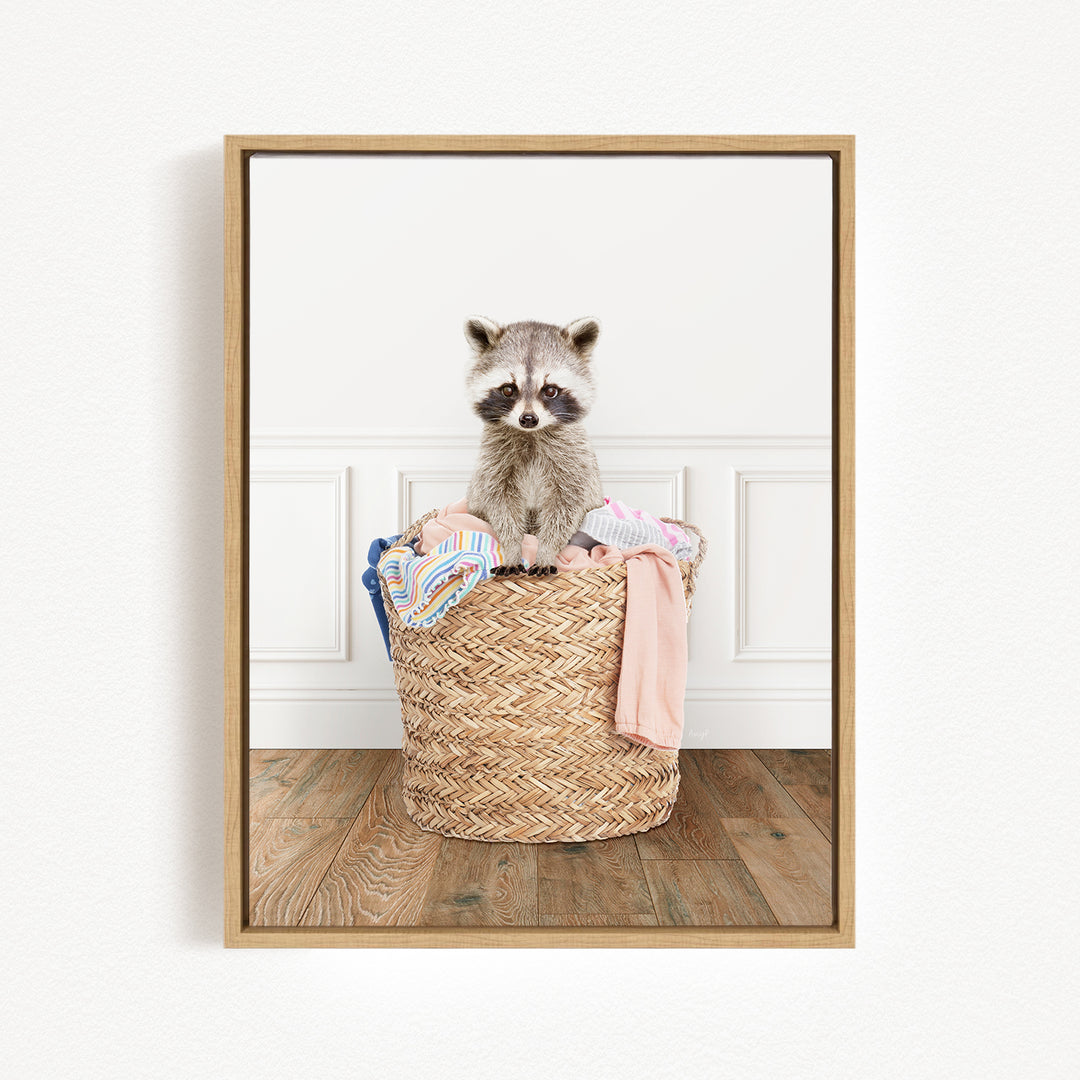 A raccoon sitting in a woven basket filled with clothes.