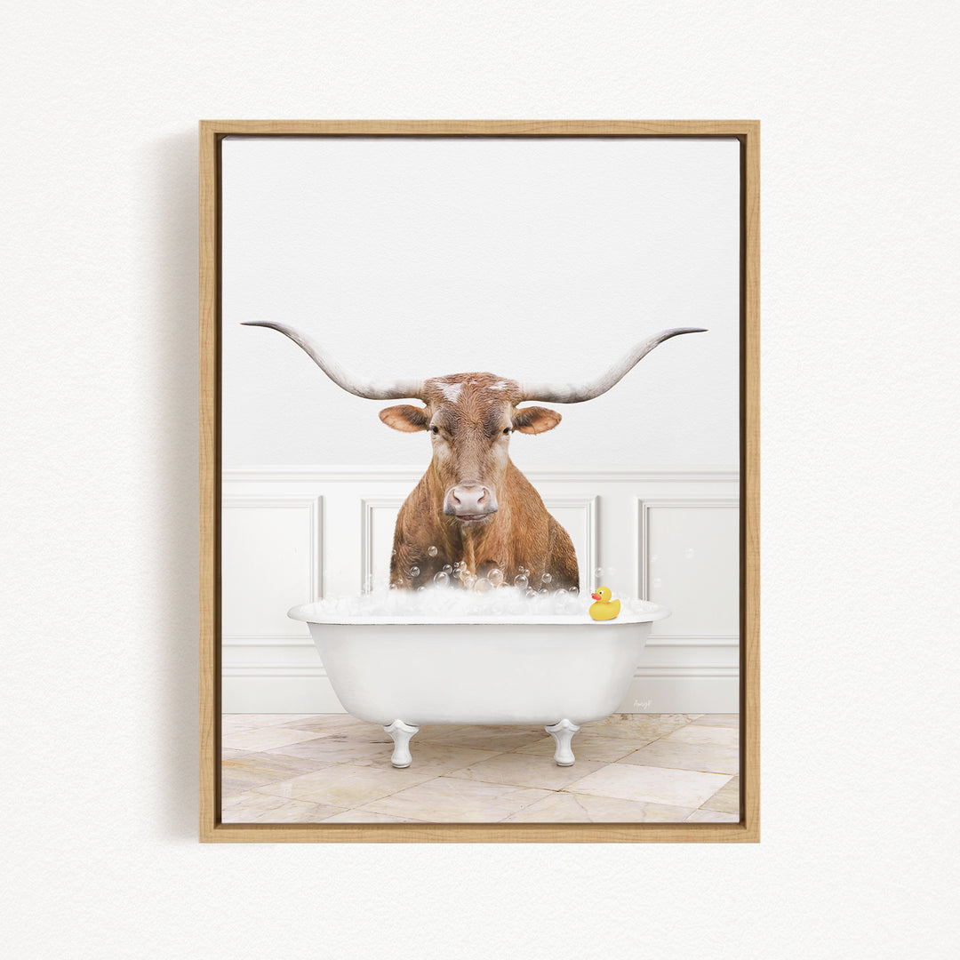 A brown cow with long horns is sitting in a white bathtub filled with bubbles, with a yellow rubber duck floating in the water.