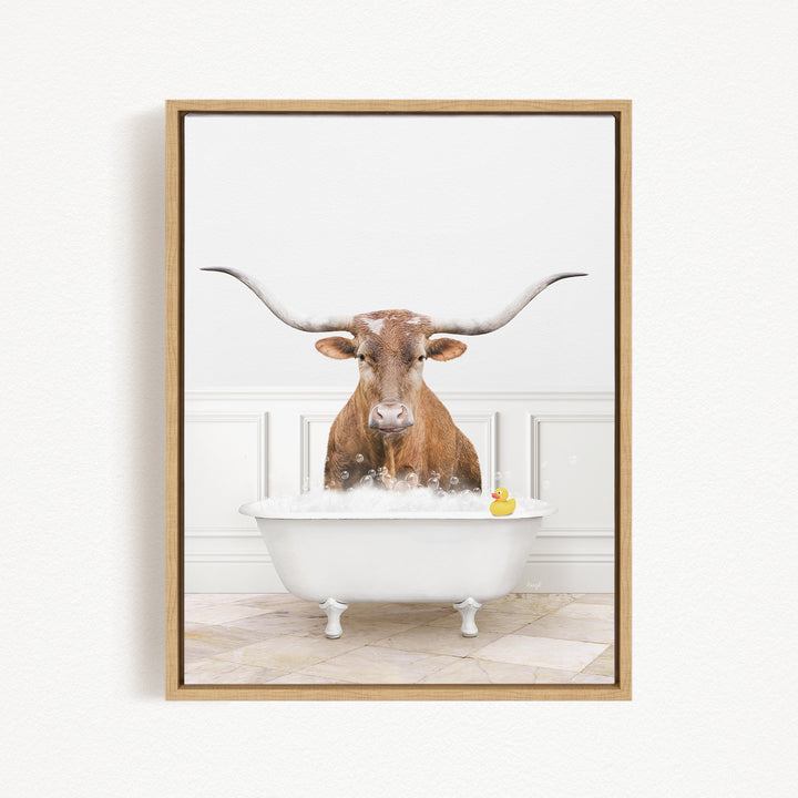 A brown cow with long horns is sitting in a white bathtub filled with bubbles, with a yellow rubber duck floating in the water.