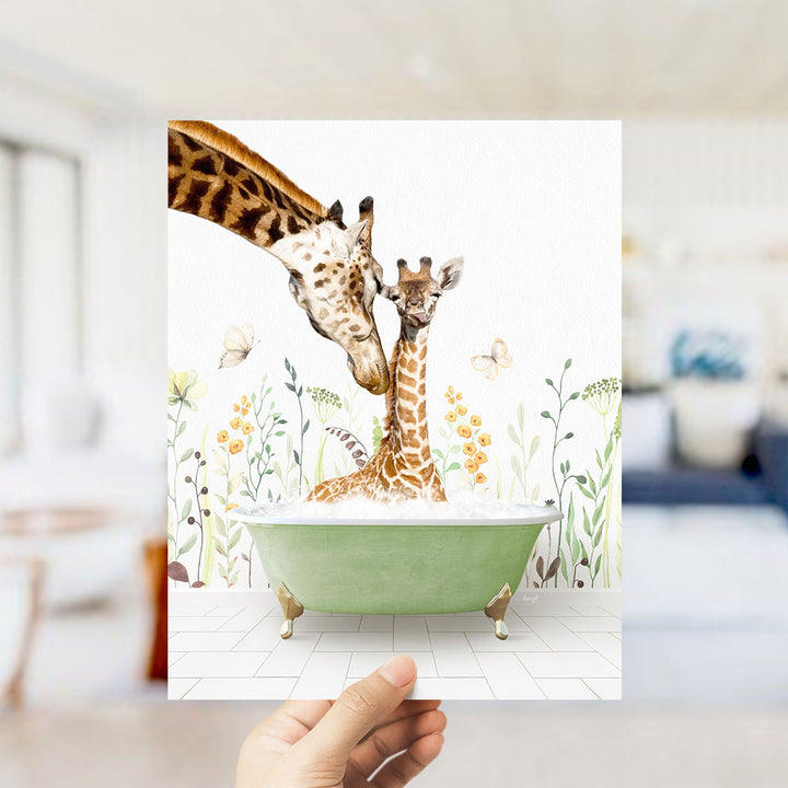 A hand holds up a framed image depicting two giraffes in a bathtub, surrounded by flowers and butterflies.
