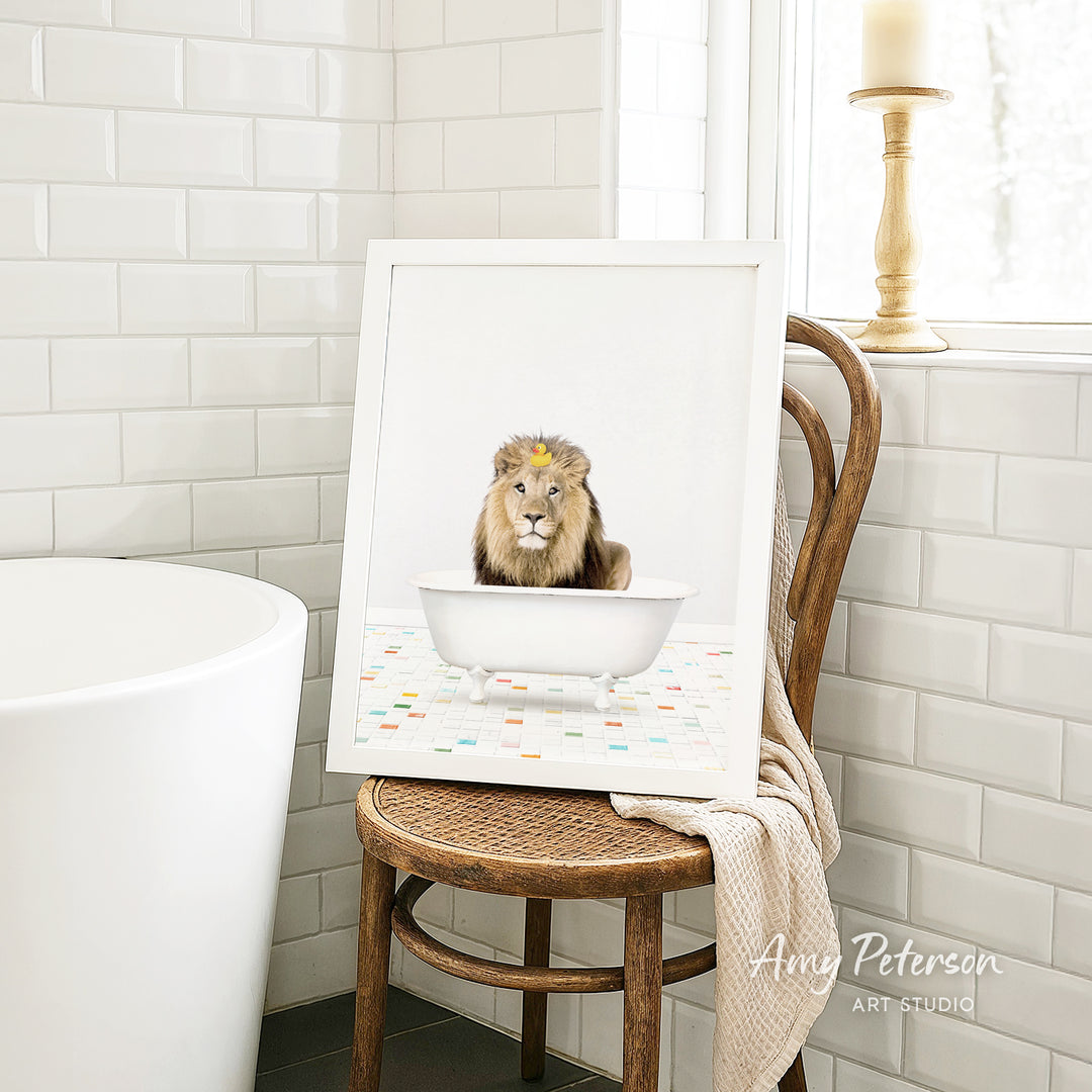 A framed image of a lion sitting in a white bathtub, with a towel draped over the back of the chair in a bathroom setting.