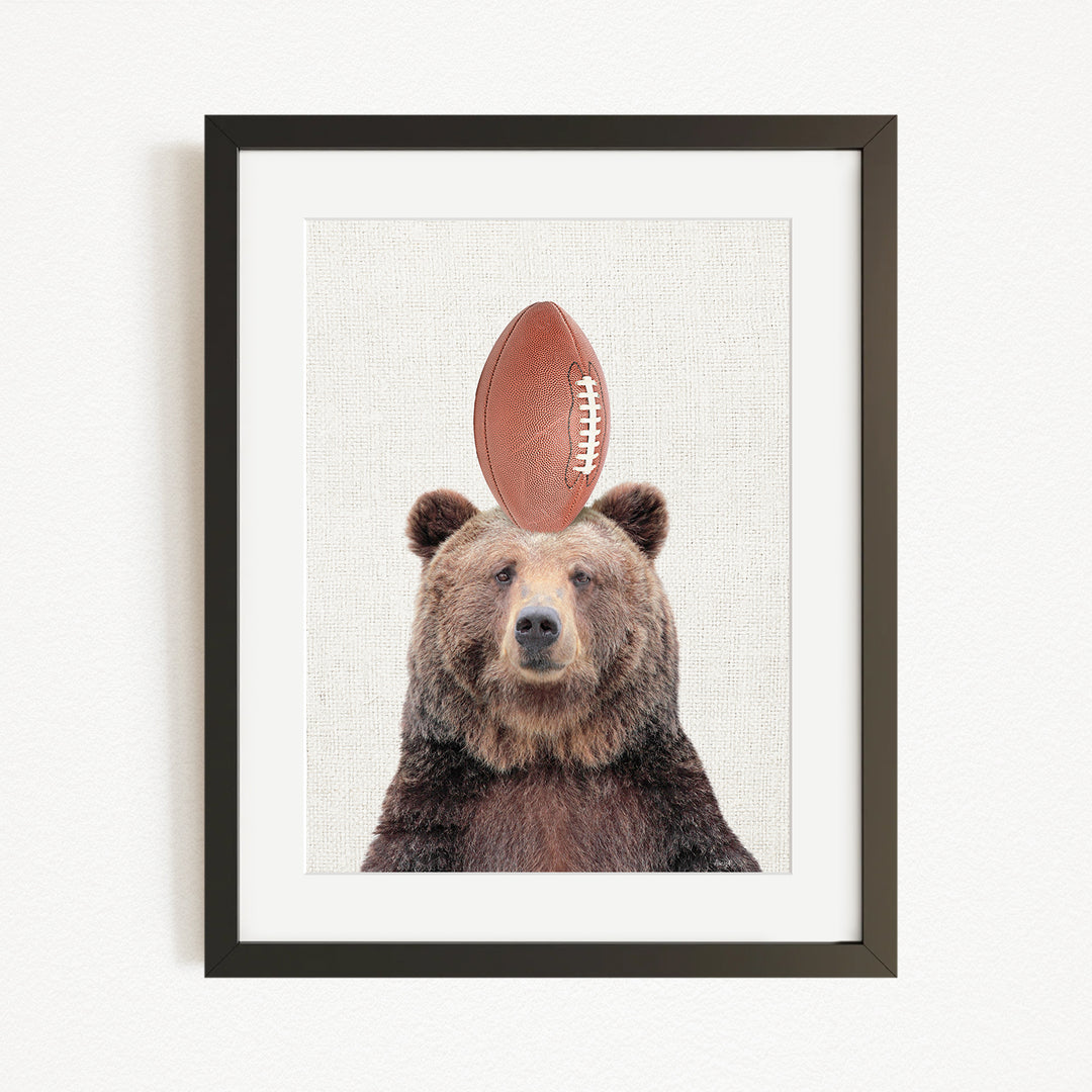 A framed image of a brown bear with a football on its head.