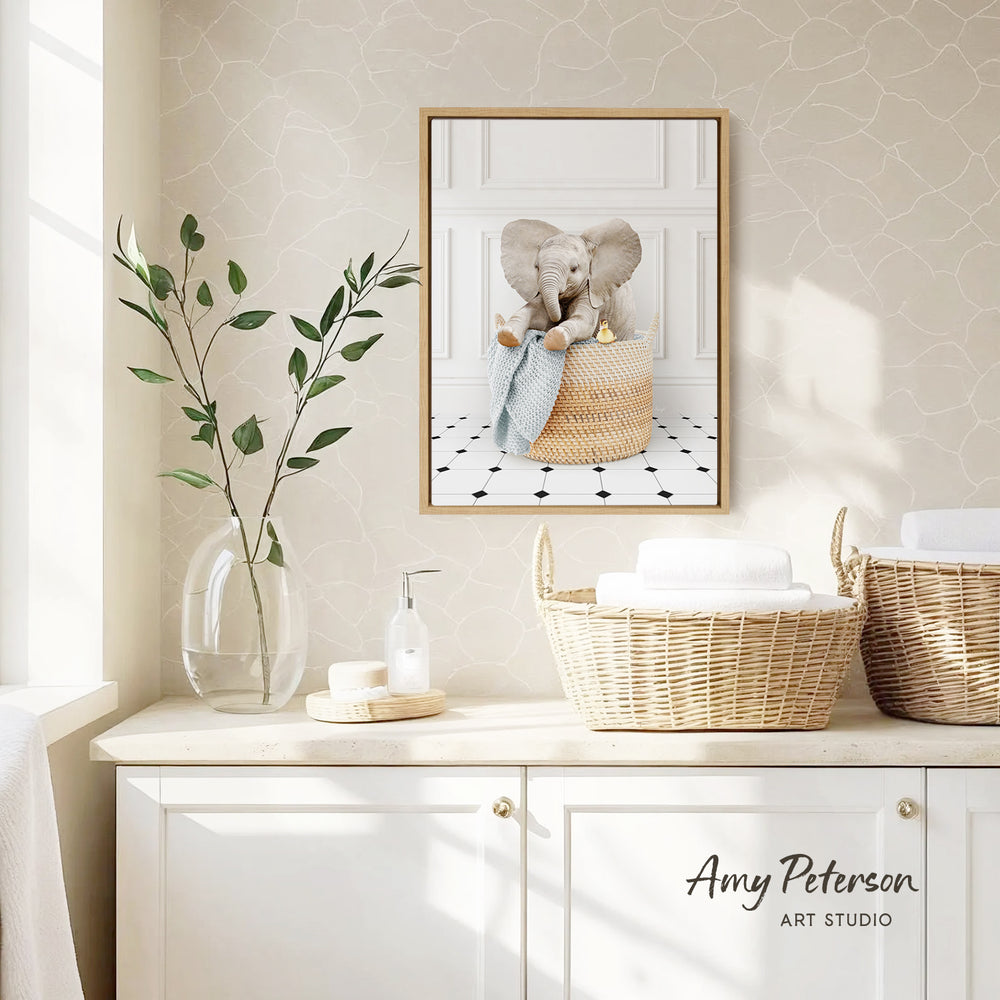 a framed picture of an elephant sitting in a basket, placed on a wall above a white cabinet with two woven baskets on top.