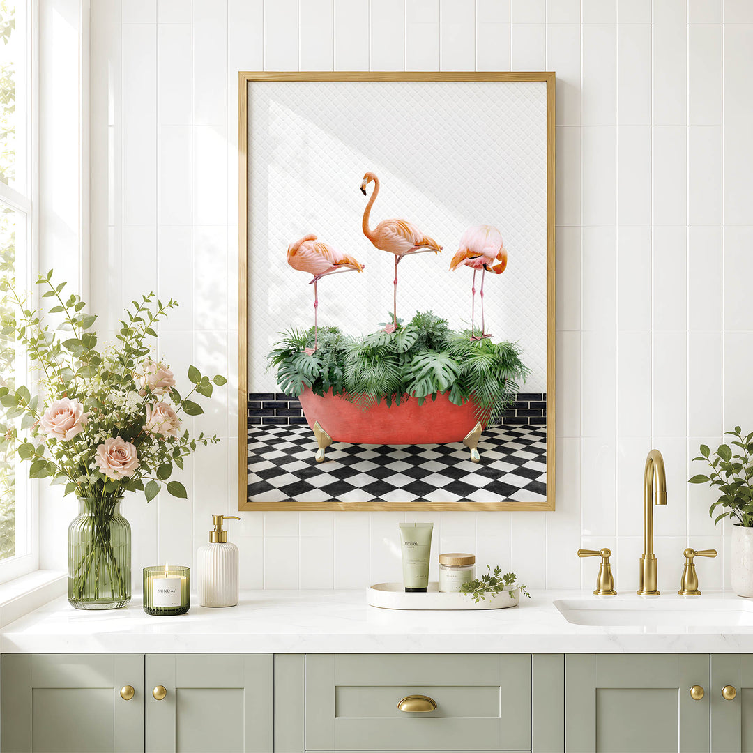 a bathroom with a framed picture of three flamingos standing in a red bathtub filled with green plants. The bathroom has a white countertop, a sink, and a vase with pink flowers.