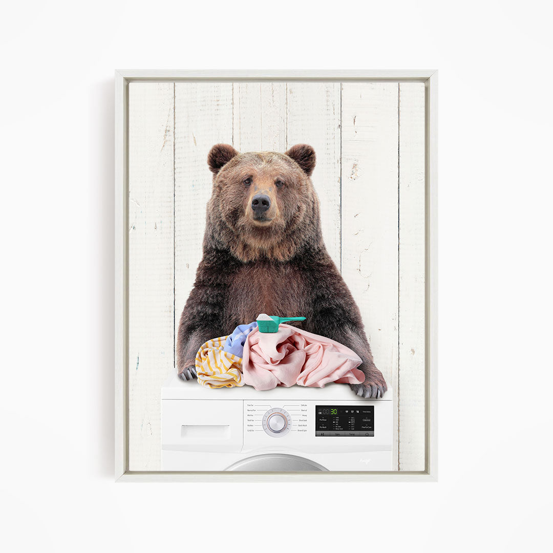 A brown bear sitting on top of a washing machine, holding a pile of clothes.