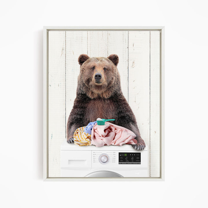 A brown bear sitting on top of a washing machine, holding a pile of clothes.