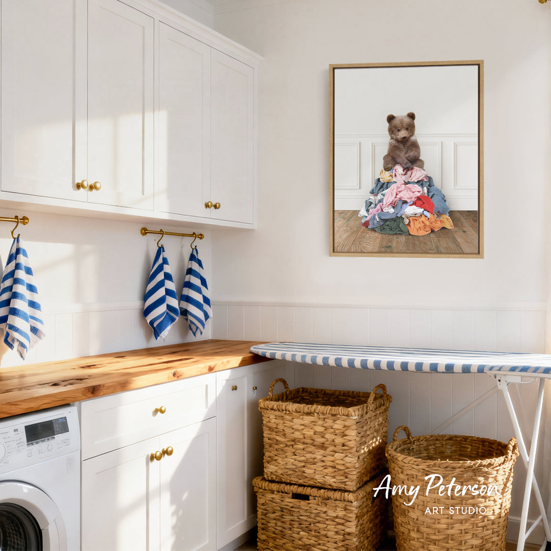 A laundry room with white cabinets, a wooden countertop, and a framed image of a bear sitting on a pile of clothes.