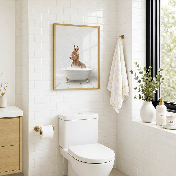 A bathroom with a white toilet, a framed picture of a dog in a bathtub, and a window with greenery on the sill.