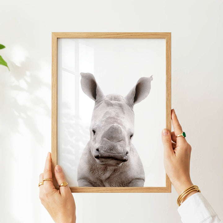A person's hands are holding a wooden frame with a picture of a rhinoceros inside it.