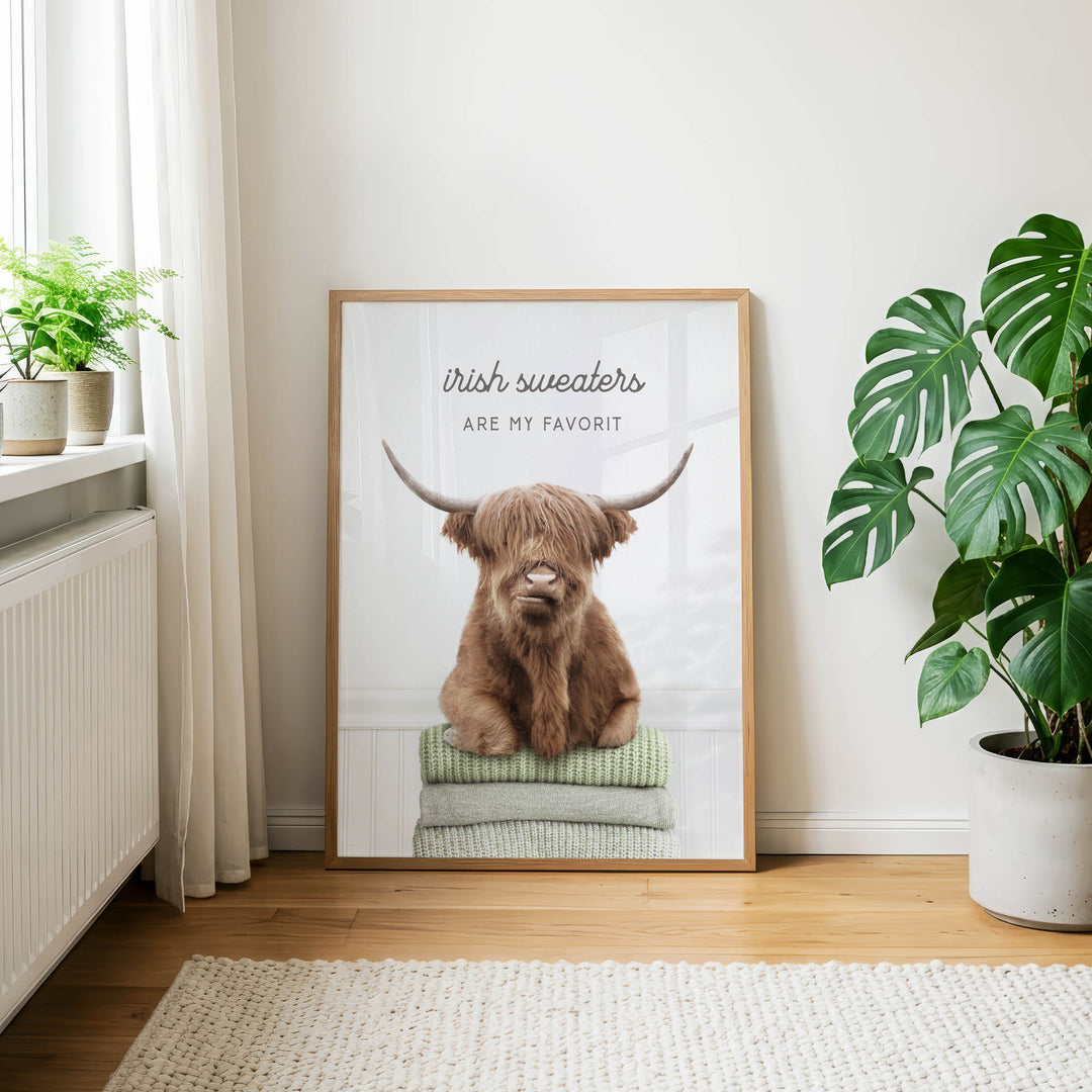 a framed poster of a brown cow with horns, sitting on a stack of green towels, with the text "Irish sweaters are my favorite" written on it.