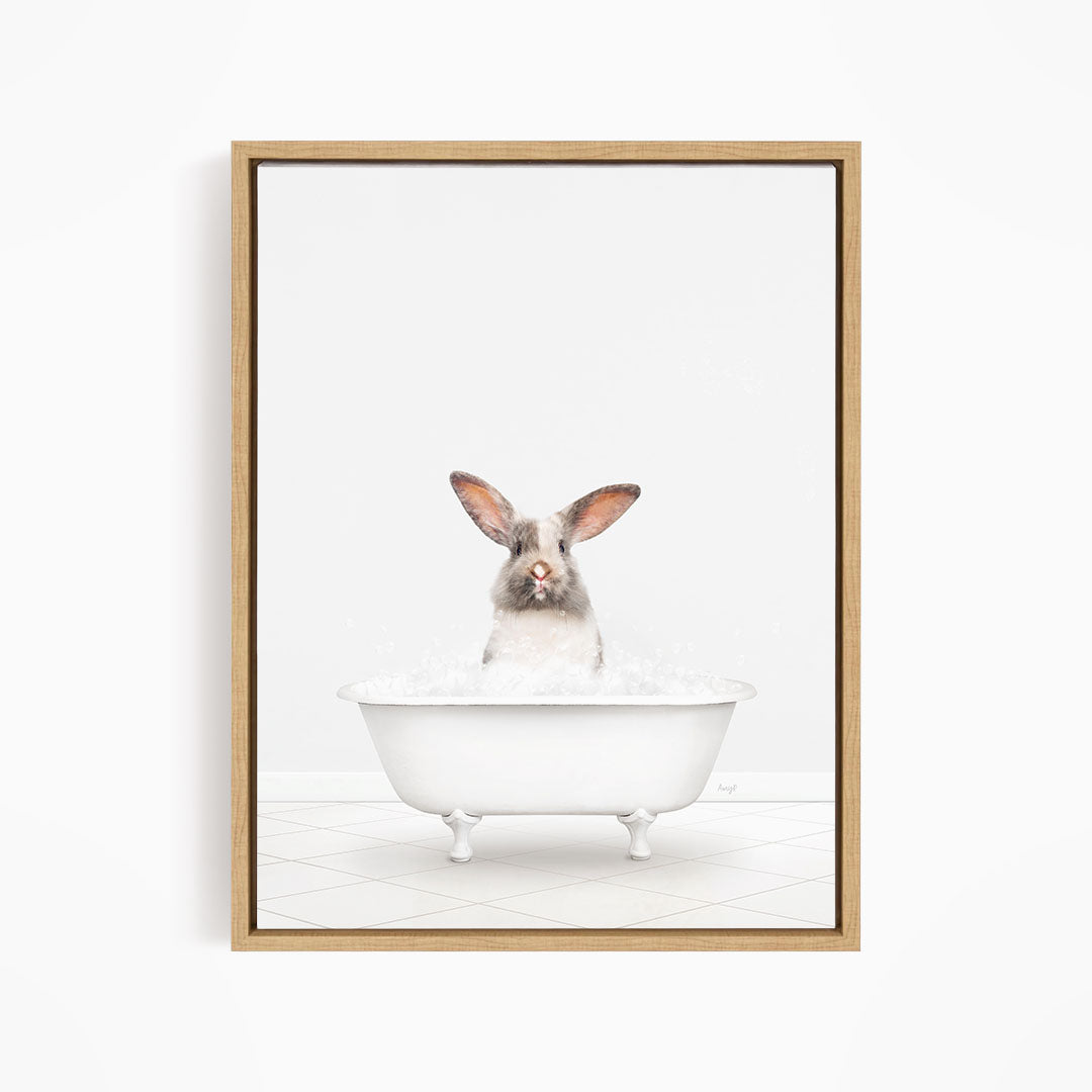A white rabbit sitting in a white bathtub filled with bubbles, looking directly at the camera.