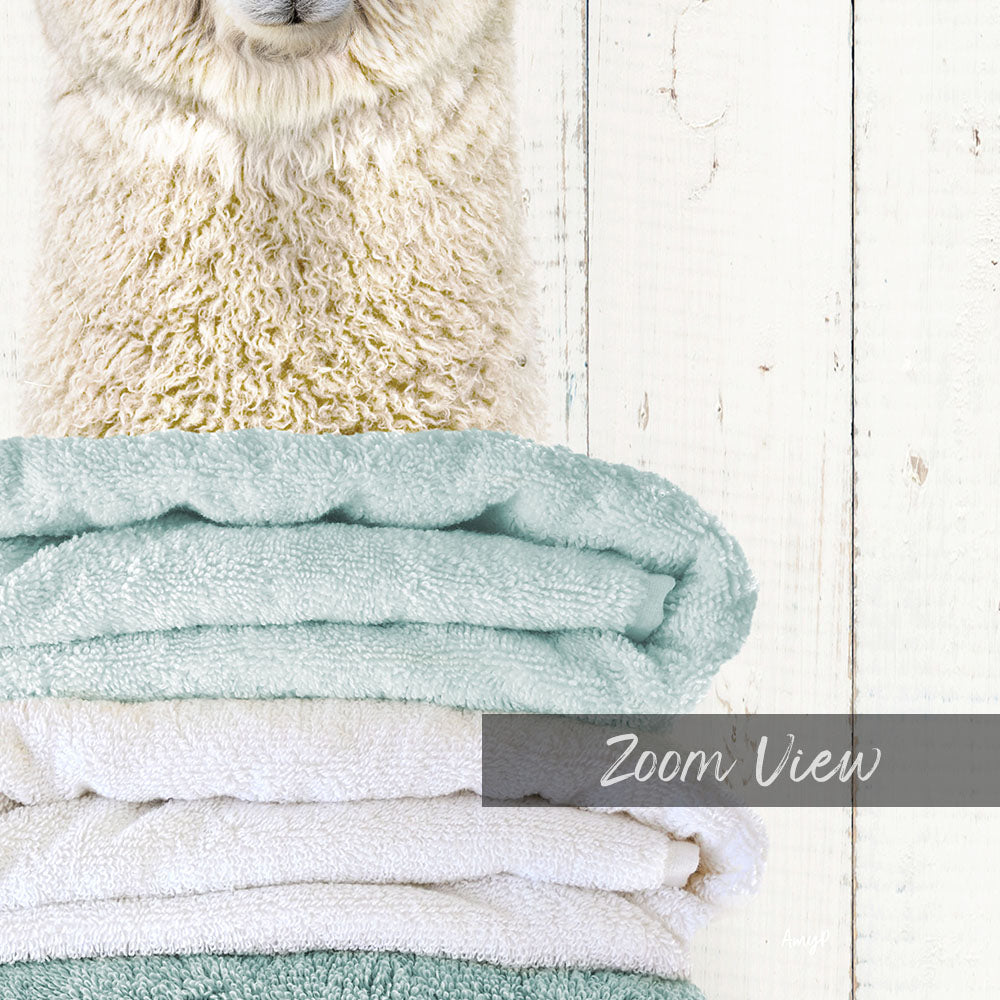 A fluffy white sheep peeking out from behind a stack of light blue and white towels, with the text "Zoom View" overlaid on the image.