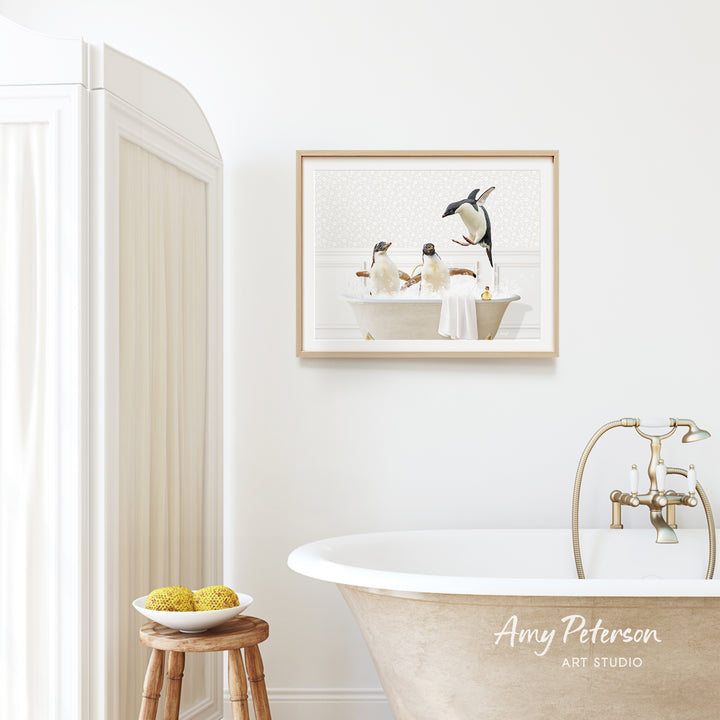 A framed image of penguins sitting in a bathtub is hanging on a white wall above a wooden stool in a bathroom.