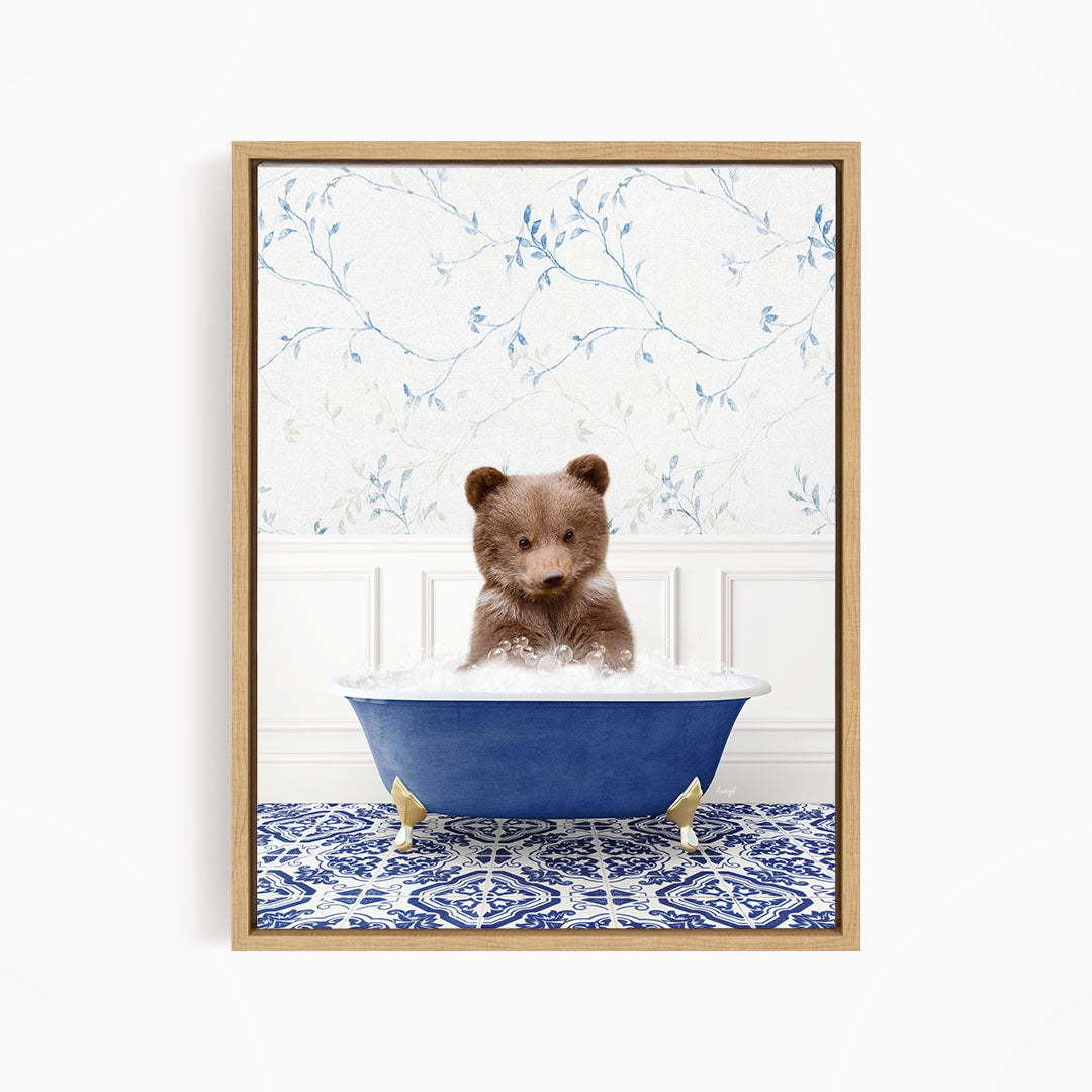 A brown bear sitting in a blue bathtub filled with bubbles, surrounded by a blue and white patterned rug and a floral wallpaper.