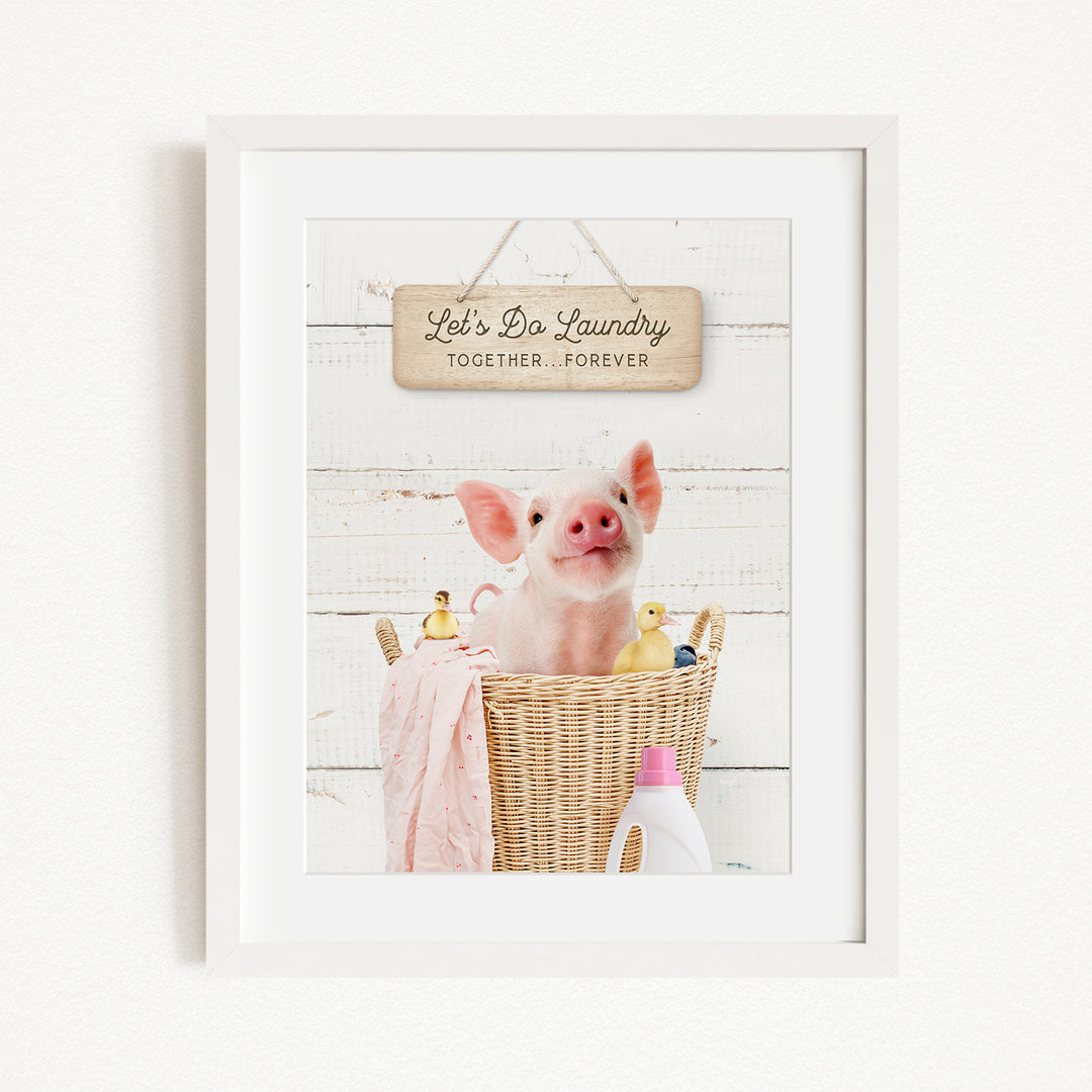 A framed image of a pig sitting in a wicker basket filled with rubber ducks, with a sign above that says "Let's Do Laundry Together Forever".