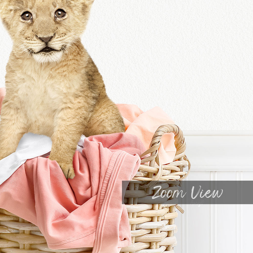 A young lion cub sitting in a wicker basket filled with pink clothing.