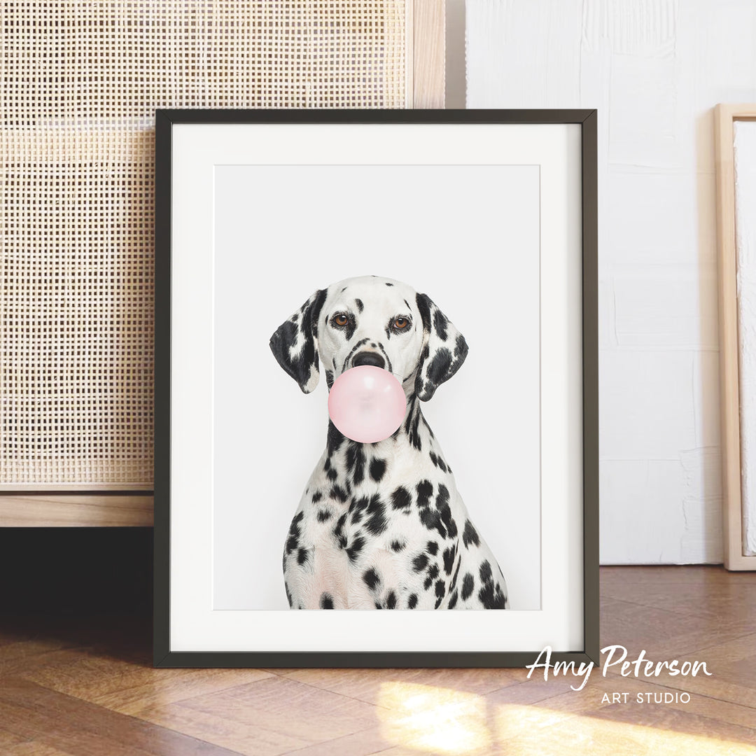 A Dalmatian dog is sitting in front of a white background, blowing a bubble with a pink bubble gum bubble.