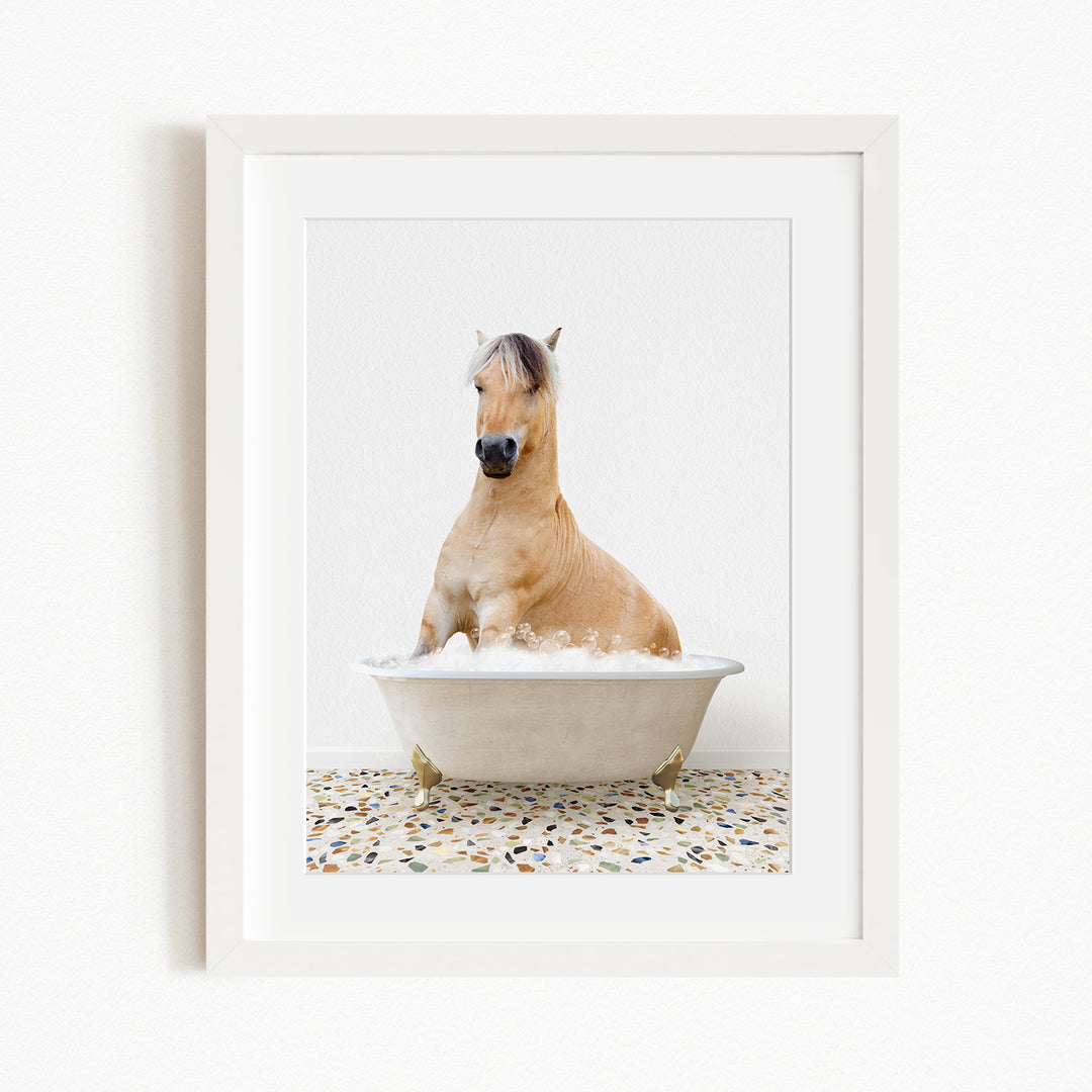 A light brown horse is sitting in a white bathtub filled with water, surrounded by a patterned floor.
