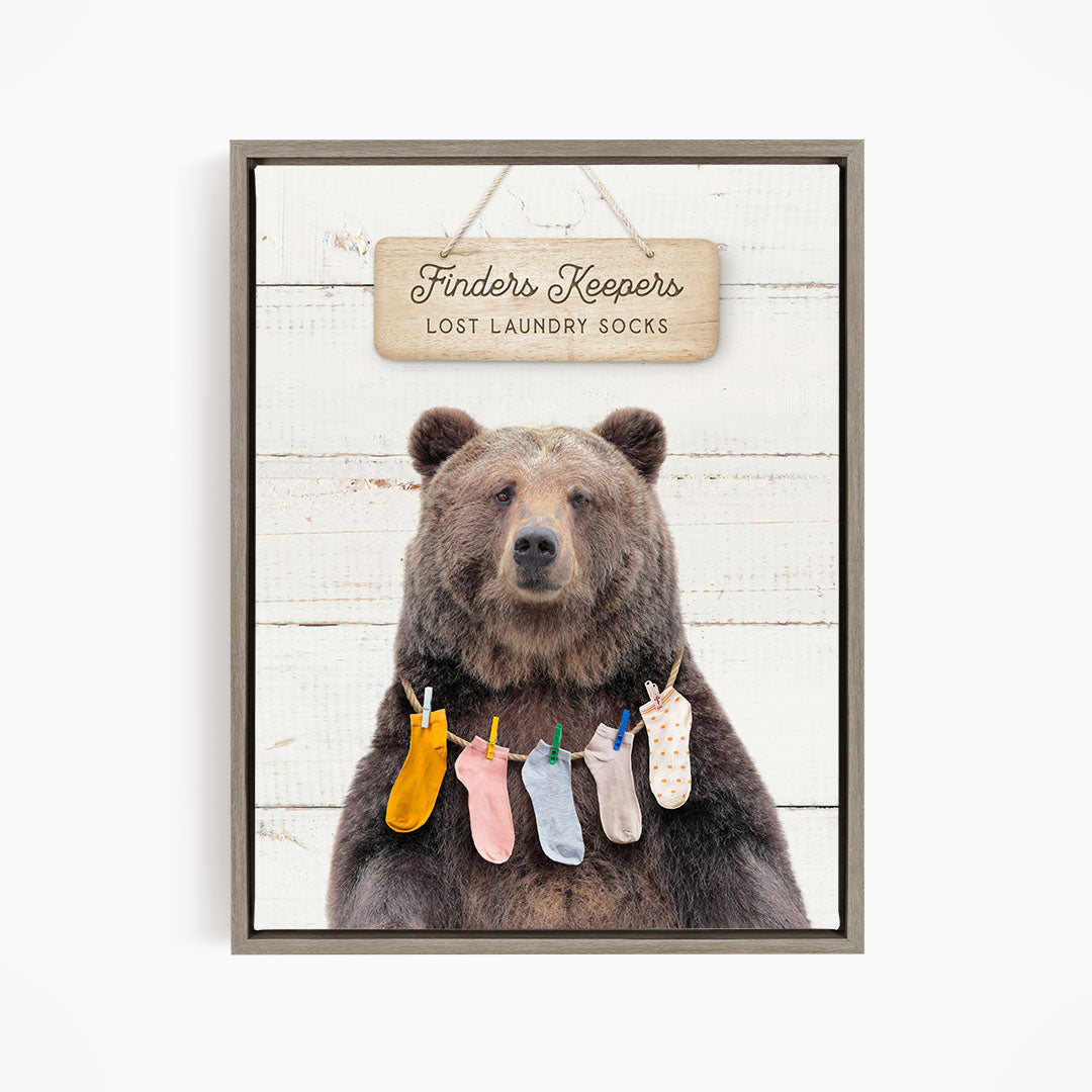 A wooden sign with the text "Finders Keepers" hangs above a bear wearing a pile of colorful socks.